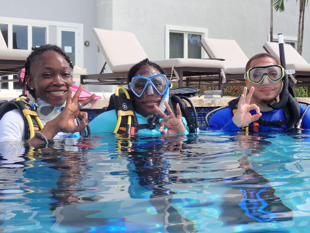 Akehia Thompson (DMR), Quetta Gibson (DMR), and Gilles Deal (DEPP) share a moment of camaraderie in their scuba gear, embarking on their training journey with smiles and determination.